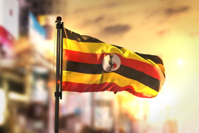 Uganda Flag Against City Blurred Background At Sunrise Backlight 3D Rendering