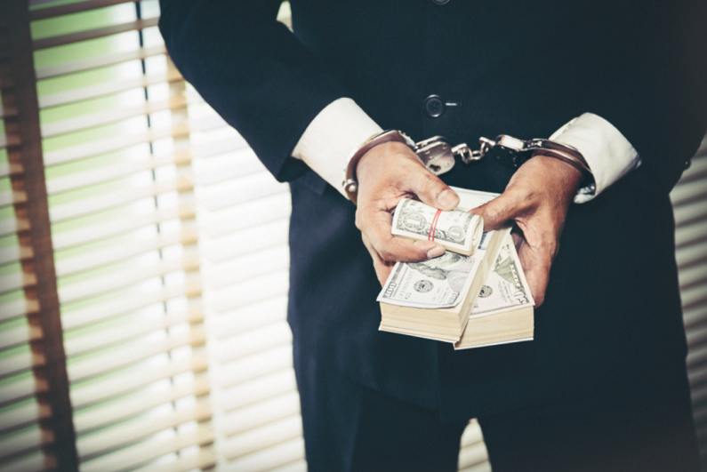 Businessman holding bundles of cash while in handcuffs.