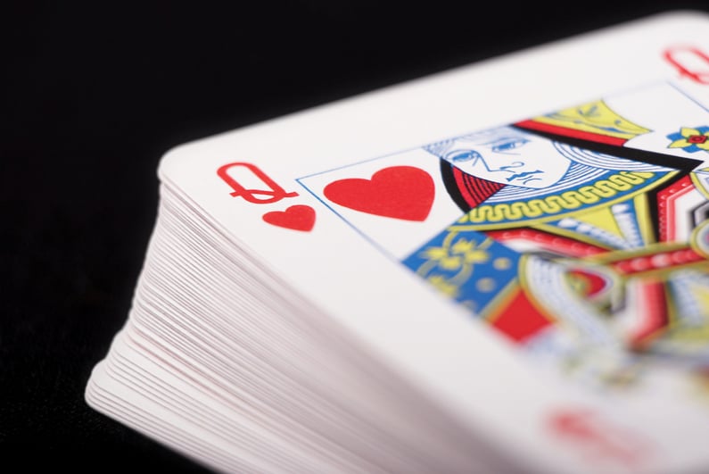 Deck of cards with Queen of hearts on top on black background