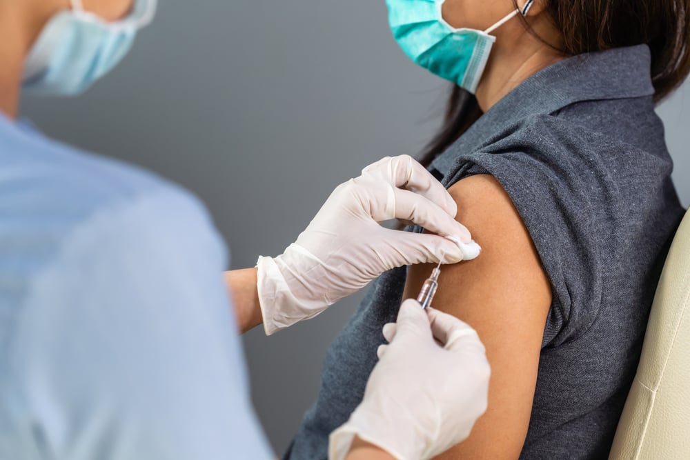 masked medical professional administers vaccine to female masked patient